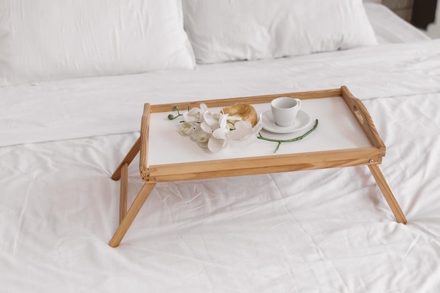 로맨틱한 아침. 격자무늬, 커피 컵, 꽃, 도넛이 있는 침대 위에 꽃이 있는 나무 커피 테이블.