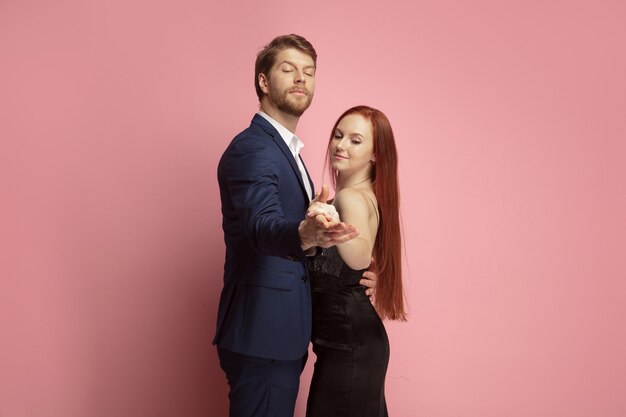 Romantic, passioned dance. Valentine's day celebration, happy caucasian couple isolated on coral studio background. Concept of human emotions, facial expression, love, relations, romantic holidays.