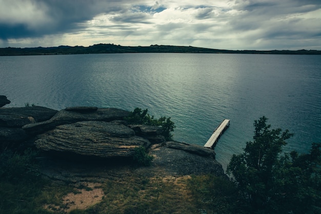 Posto romantico sul lago con molo di legno sulla riva rocciosa