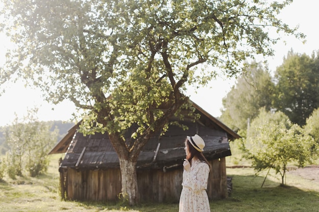 Romantic portrait of a young woman in straw hat and beautiful dress in the countryside in summer