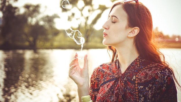 Romantic portrait of young woman with soap balloons. Sunny Valley and river on a summer day