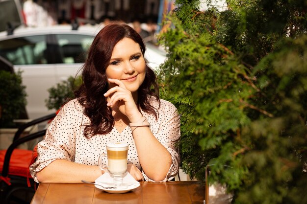 Romantica donna di mezza età dai capelli rossi con i capelli ricci seduto al caffè di strada con una tazza di caffè. spazio per il testo