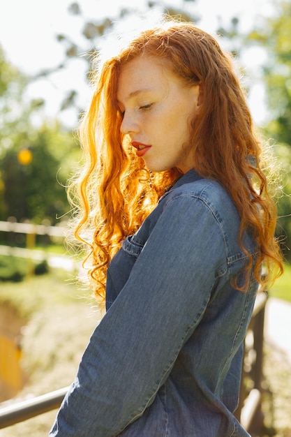 Romantic redhead young woman in denim shirt posing  in rays of sun at the forest