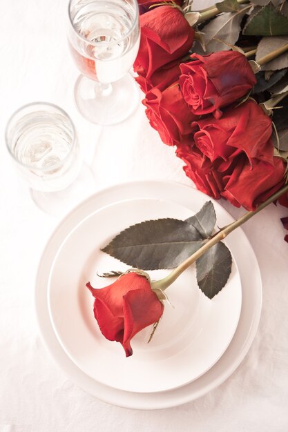 Romantic restaurant table setting for two with roses, plates and glasses.
