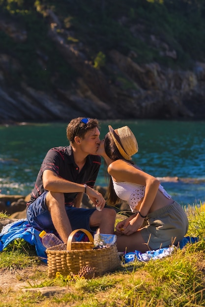 Scena romantica di una coppia che si bacia durante il picnic in montagna in riva al mare a godersi il caldo