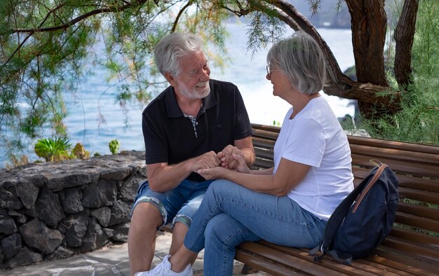 Romantic senior couple hands in hands sitting outdoor under a tree looking into each other eyes