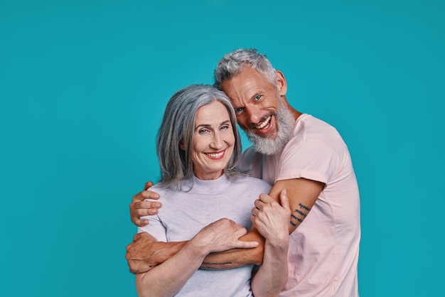 romantic senior couple looking at camera and smiling while standing together against blue background