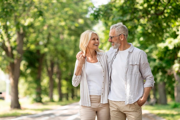 Romantic senior couple walking outdoors in summer park and embracing