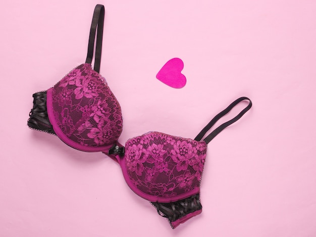 Concetto sessuale romantico. bellissimo reggiseno sexy, cuore decorativo su sfondo rosa. vista dall'alto, minimalismo