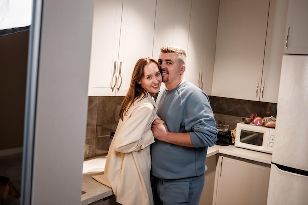 Романтическая сексуальная молодая пара счастливо проводит время, обнимаясь и целуясь в уютной современной кухне дома. Два человека стоят и радостно смотрят друг на друга.