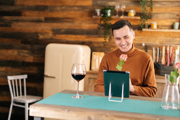 Romantic smiling young man presents beautiful flower through tablet to his girlfriend during online communication. Male using tablet computer and having online video chat.