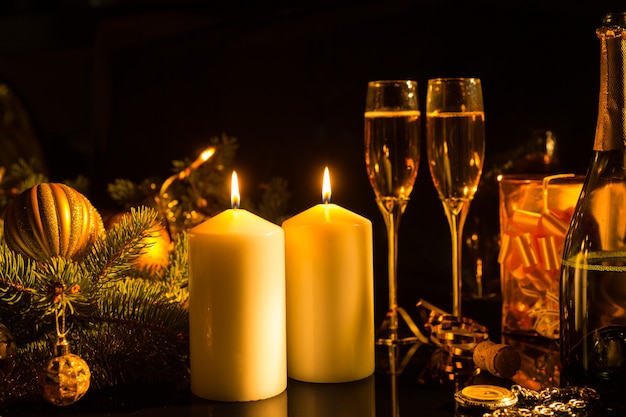 Romantic Still Life of Lit Candles Illuminating Glasses of Champagne on Dark Background with Christmas Decorations and Gifts - Sentimental Image of Festive Burning Candles in Warm Light