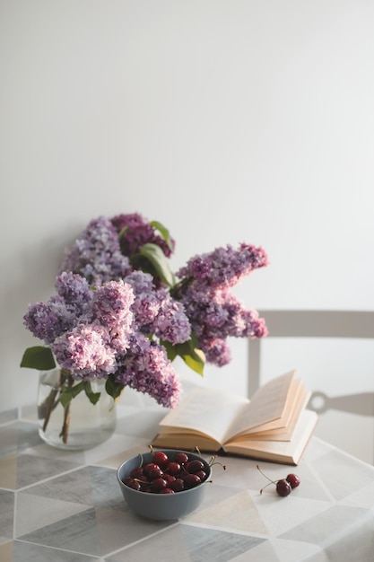 Romantic still life with an open book lilac flowers and cherries on a table