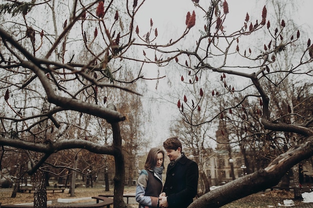 Romantic stylish couple hugging gently holding hands in autumn park under unusual tree man and woman embracing family togetherness concept calm atmospheric moment