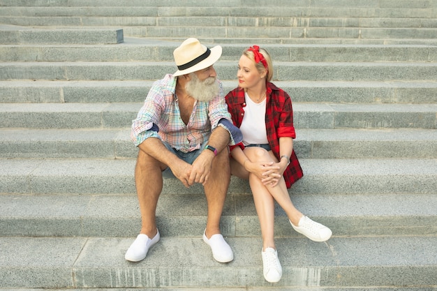 Romantic tourist couple sitting on stairs. bearded senior man and young woman.