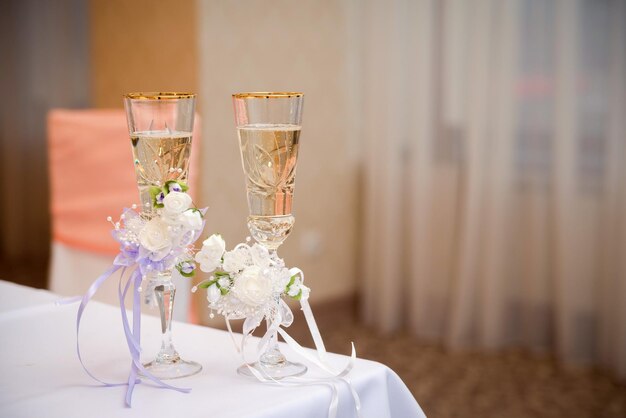 Romantic view of wedding glasses with champagne on white tablecloth in the restaurant Two crystal glasses with sparkling champagne decorated with white flowers Closeup