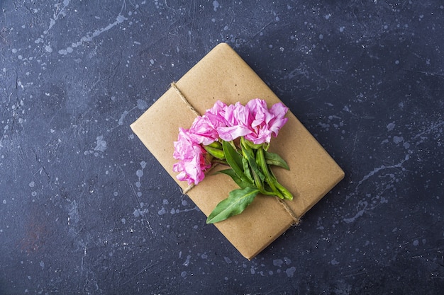 Romantica natura morta vintage con graziosa confezione regalo avvolta con carta artigianale e decorata con fiori rosa su sfondo scuro