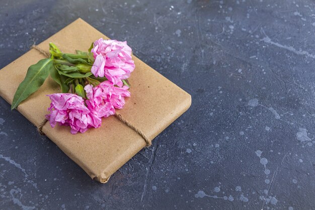 Romantic vintage still life with pretty gift box wrapped with craft paper and decorated with pink flower on dark background