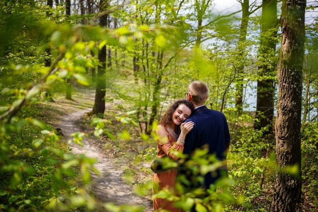 Romantic walk of a young couple in a green forest, warm spring weather. Guy and girl hugging in nature