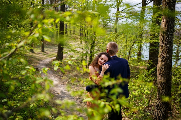 Romantic walk of a young couple in a green forest, warm spring weather. Guy and girl hugging in nature