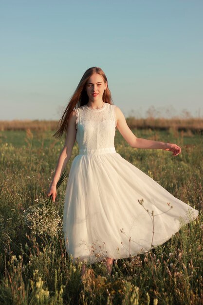 Romantic woman dancing in a wonderful flower field Warm sunset colors White dress Soft colors