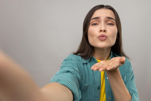 Romantic young adult woman making point of view photo sending air kissing POV expressing love and gentle wearing casual style jacket Indoor studio shot isolated on gray background