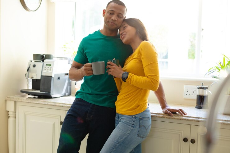 Romantic young african american couple leaning on kitchen counter while holding coffee mugs. people, love and togetherness concept, unaltered.