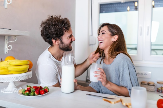 Giovani coppie romantiche che cucinano insieme in cucina, divertendosi insieme. uomo e donna che ridono e bevono latte al mattino a colazione