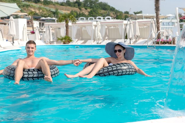 夏休みの日差しを楽しんでいるゴム製のチューブに並んで浮かぶプールで手をつないでロマンチックな若いカップル