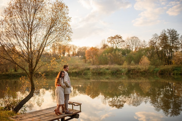 A romantic young couple stands on a pier near the lake. Fall.