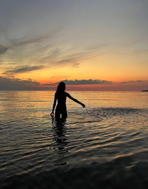 romantic young woman  silhouette at orange sunset in the sea water wave and pink cloudy sky