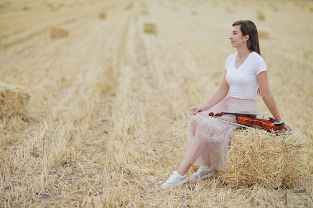 Romantic young woman with flowing hair holding a violin in her hand in a field