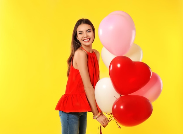 Giovane donna romantica con palloncini a forma di cuore per san valentino su sfondo colorato