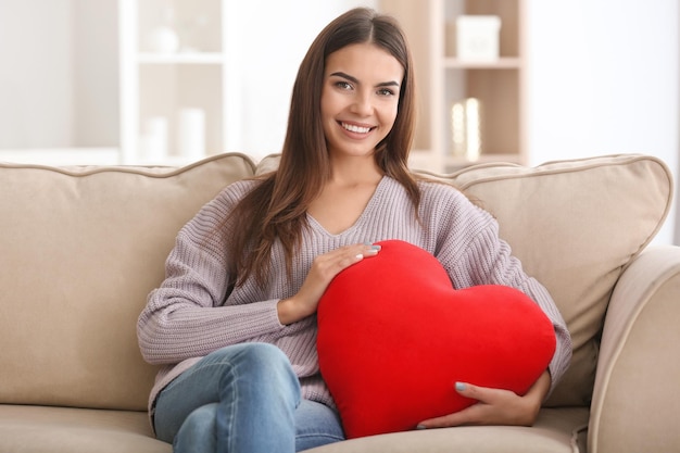 Giovane donna romantica con cuscino a forma di cuore a casa
