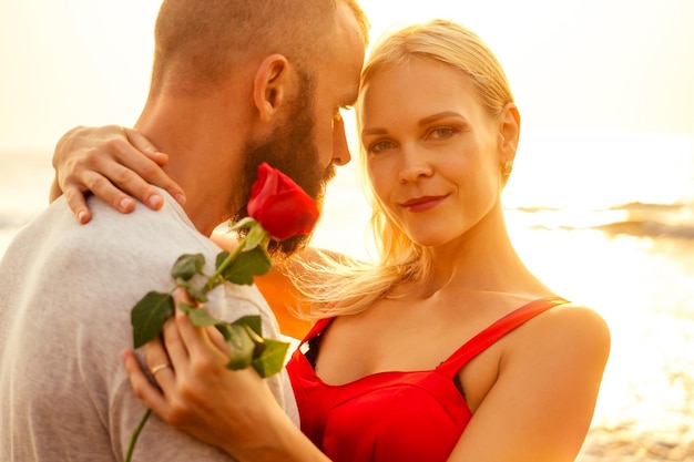 Romantisch 14 februari Valentijnsdag zomervakantie relatie datingliefde paar met boeket bloemen man in een wit overhemd en een blonde vrouw in een lange jurk met een roos in zijn hand op het strand