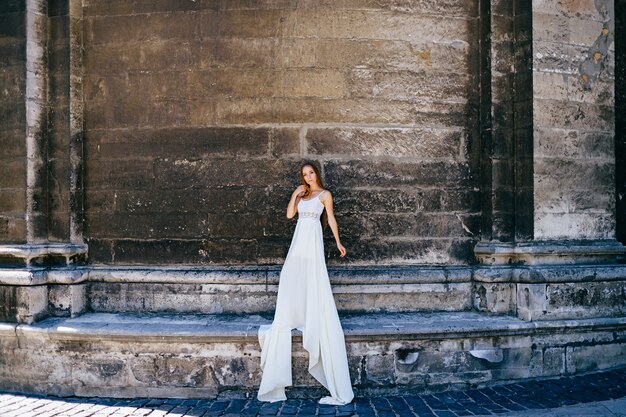 Romantisch elegant meisje in lange witte jurk poseren over oude stenen muur