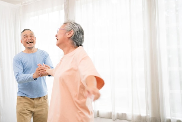 Romantisch en vrolijk Aziatisch welzijn senior koppel geniet van dansen en hand in hand op muziek samen met een glimlach en geluk in de woonkamer Senior pensioenactiviteit thuis