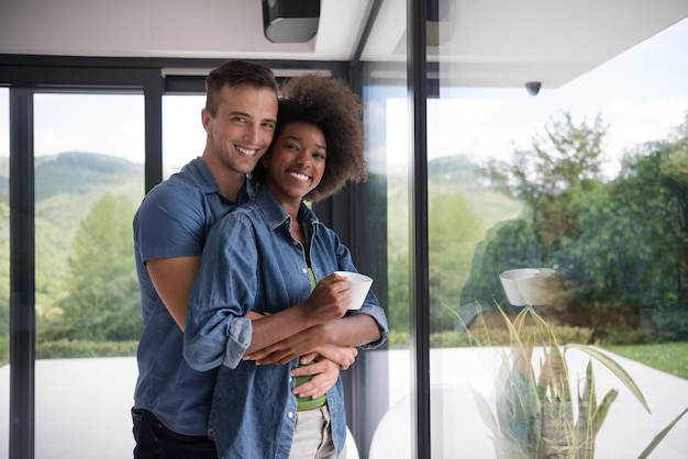 romantisch gelukkig jong multi-etnisch koppel genietend van koffie in de ochtend bij het raam in hun luxe huis