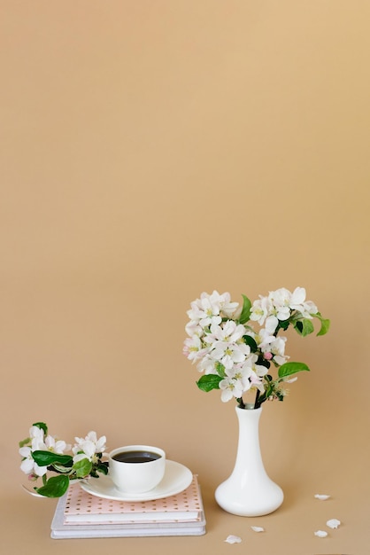 Romantisch lentestilleven op een beige achtergrond een vaas met witte appelbloesems een kopje thee in een wit porseleinen kopje en boeken