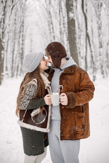 Romantisch paar dat in het winterbos staat en twee kopjes met cacaodrank vasthoudt