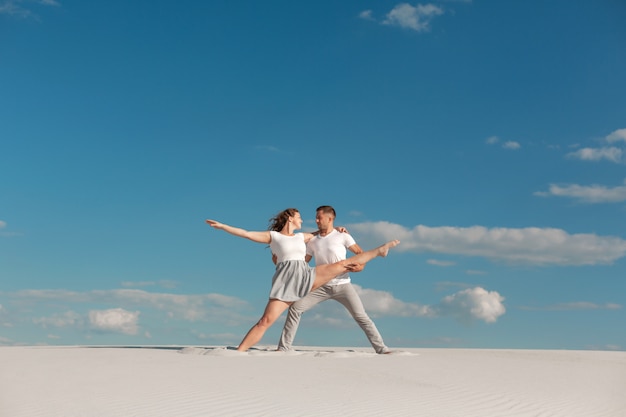 Romantisch paar dat in zandwoestijn bij blauwe hemelachtergrond danst