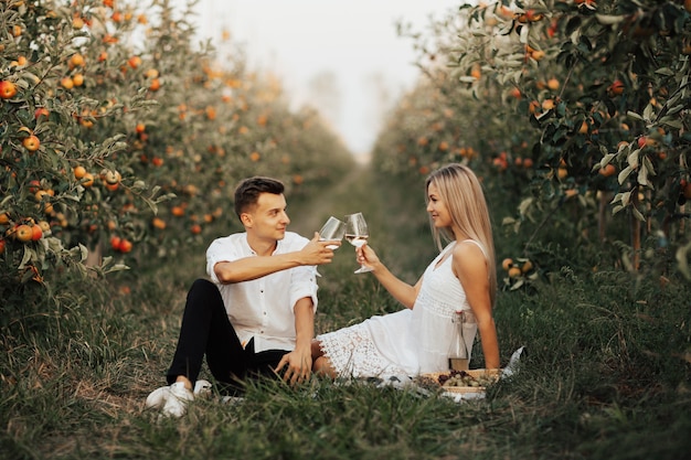 Romantisch paar rammelende glazen met witte wijn zittend op een picknick in de natuur.