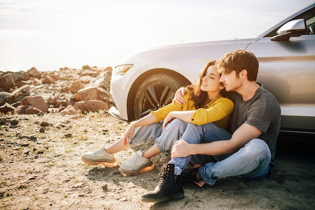 Romantisch paar staat in de buurt van een Muscle car op het strand. De knappe bebaarde man en een aantrekkelijke jonge vrouw hebben een liefdesverhaal.