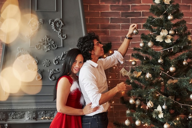 Romantisch paar verkleden kerstboom in de kamer met bruine muur en open haard.