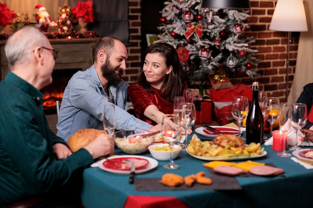 Romantisch paar vieren kerst met familie, gelukkige vriend en vriendin praten aan feestelijke tafel. Kerstviering, vrouw en man eten traditionele maaltijd met ouders