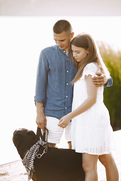 Romantisch paar vriend en vriendin wandelen samen met rotweiller hond in de buurt van het meer. Man en vrouw kijken naar hun hond