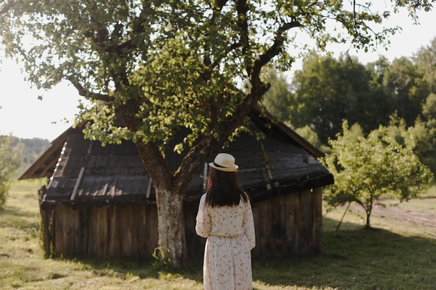 Romantisch portret van een jonge vrouw in strohoed en mooie jurk op het platteland in de zomer