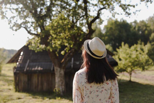 Romantisch portret van een jonge vrouw in strohoed en mooie jurk op het platteland in de zomer