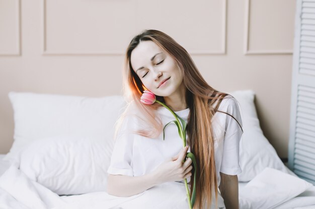 Romantisch portret van een mooie gelukkige jonge vrouw in bed met verse roze tulpen