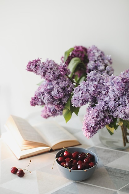 Romantisch stilleven met een open boek lila bloemen en kersen op een tafel